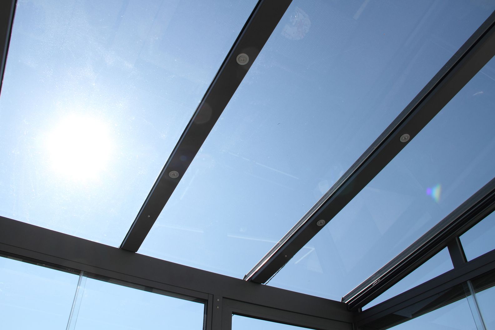 Moderne Glaskonstruktion mit schwarzen Rahmen und großflächigen Glaselementen unter blauem Himmel